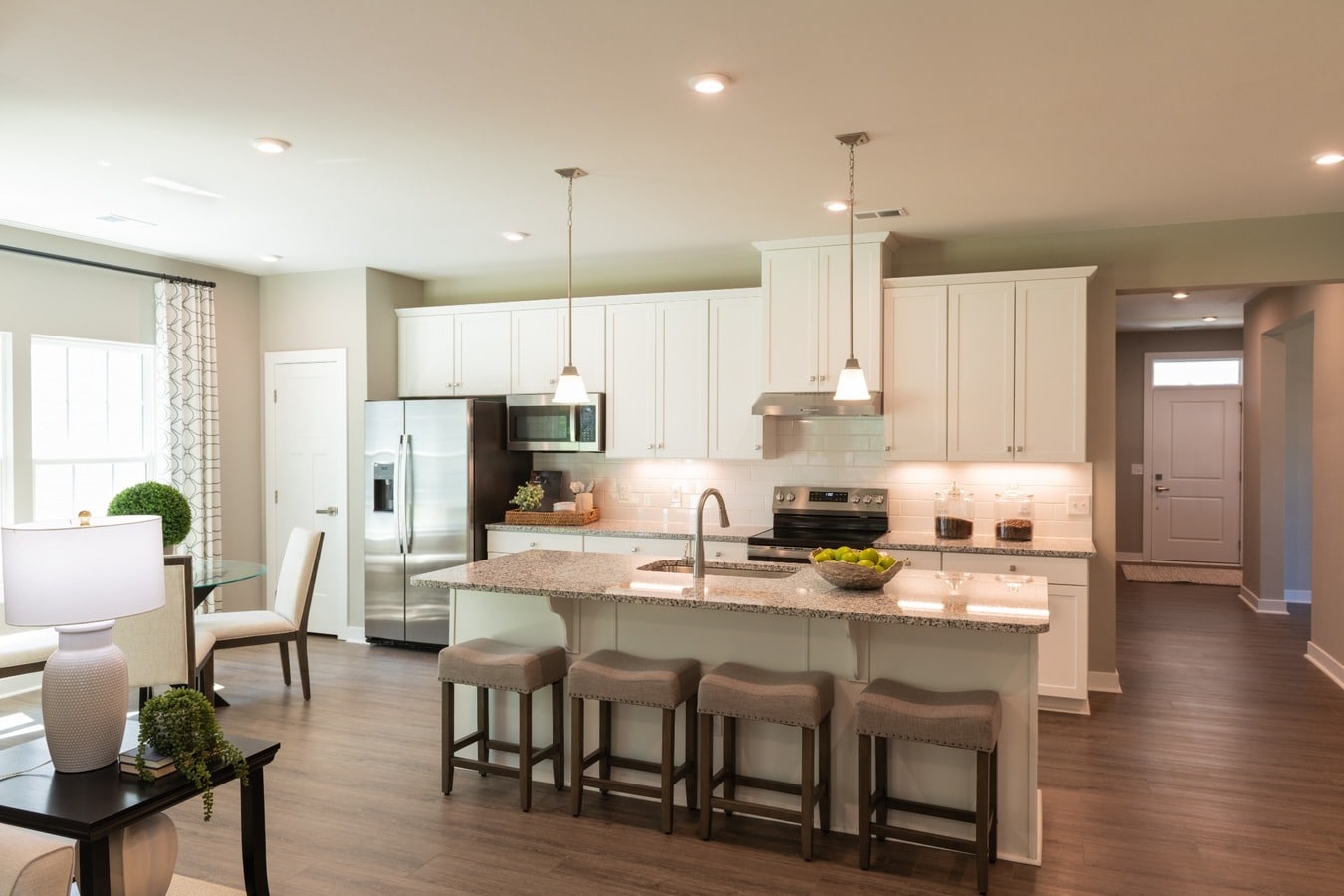 Modern open concept kitchen with white cabinetry, granite countertops, stainless steel appliances, large center island, and breakfast bar seating in a spacious Florida home.