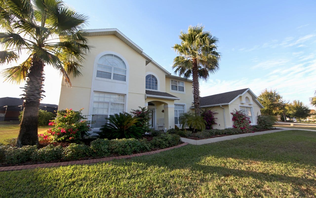 Beautiful Palm Tree Lined Family Home Two story residential home with palm trees, flowering shrubs, and manicured landscaping under a bright blue sky.