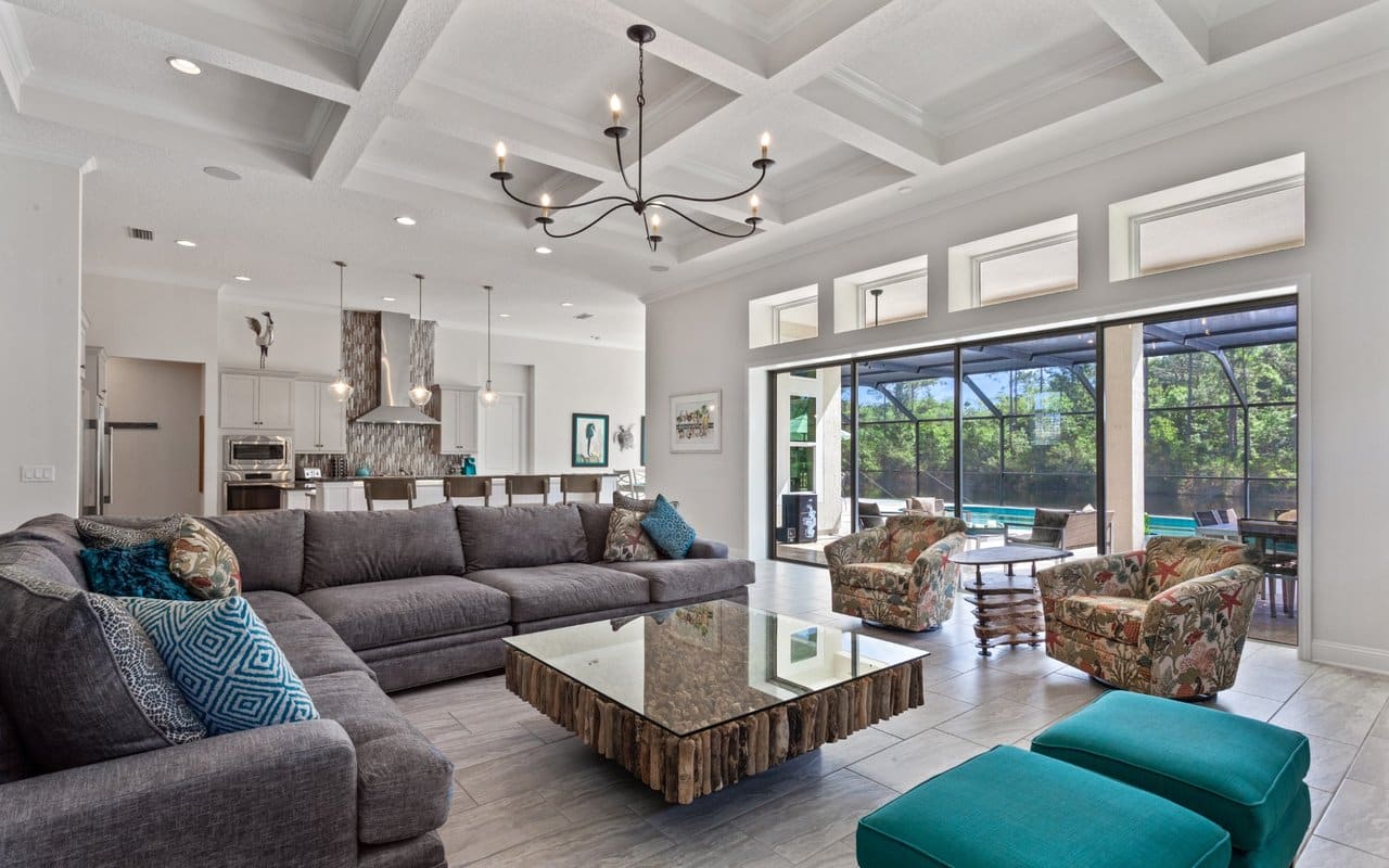 Luxury Open Concept Living Room Spacious living room with sectional sofa, coffered ceiling, modern kitchen, and pool views through large glass doors.