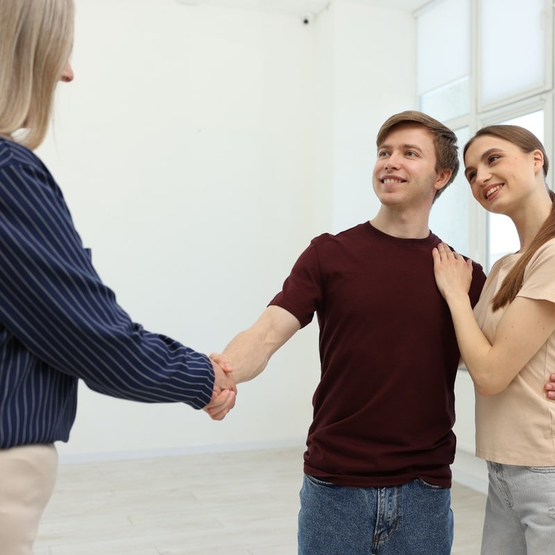 Young Couple Meeting Real Estate Agent in Empty Home Titusville FL real estate agent shaking hands with a young couple during a home viewing in a residential property.